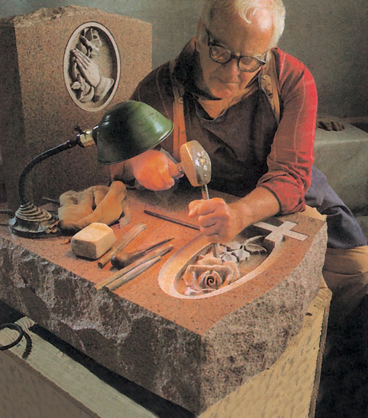 A Rock of Ages stone artisan hand carves a rose into a granite headstone 