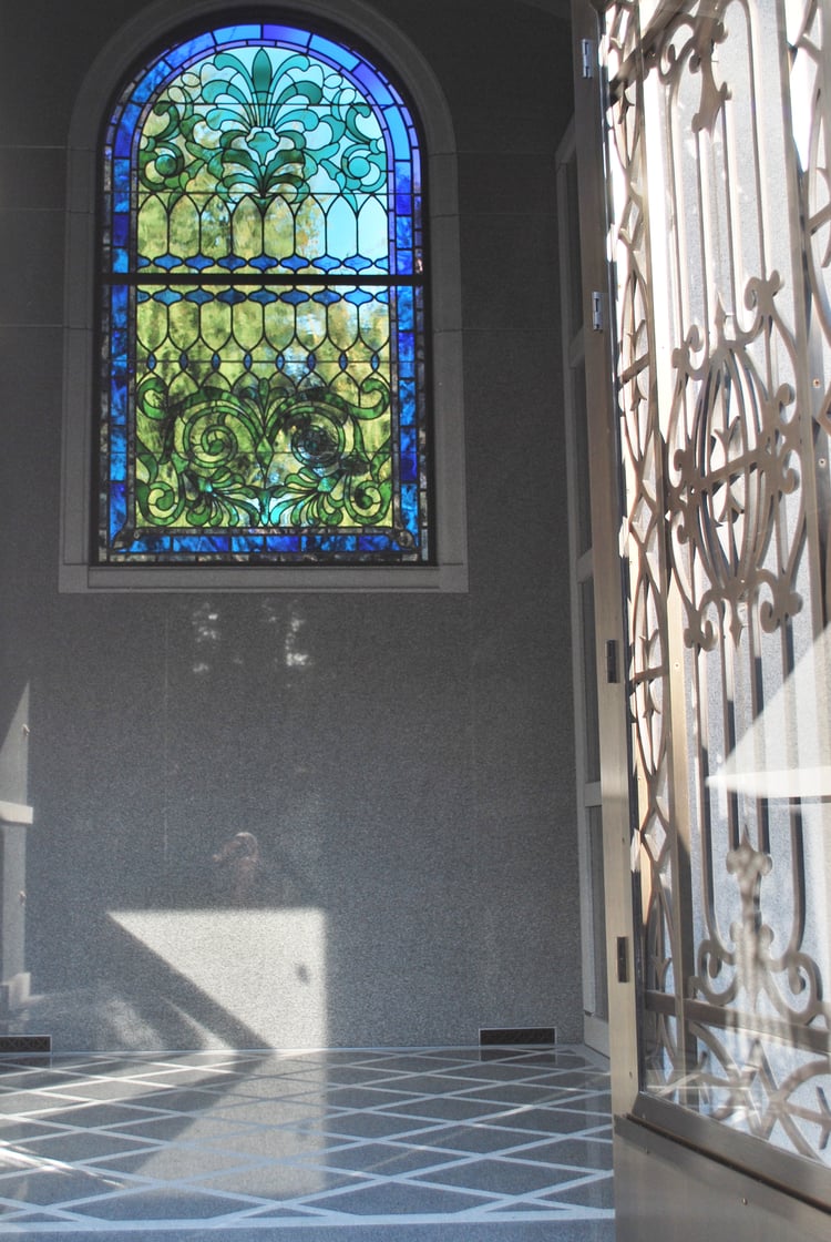 Stained glass windows reflect light on detailed carvings on Blue Gray Granite Mausoleum